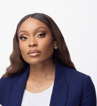 Stephanie Ike, with long brown hair, in a navy blazer over a white top and a fine pendant necklace, looking into the camera against a white backdrop.